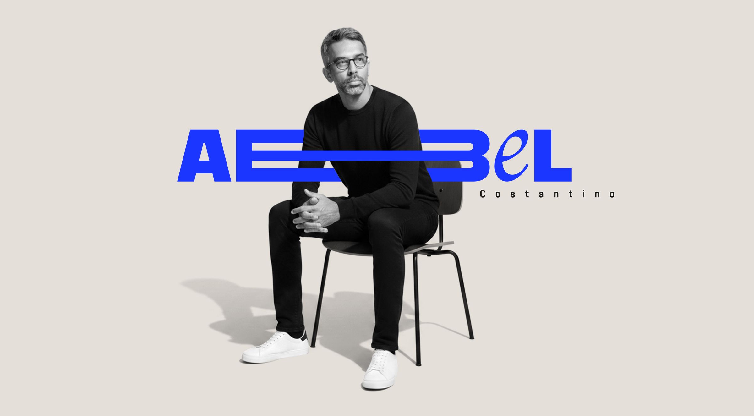 Ritratto in bianco e nero di un uomo seduto su una sedia, con il logo blu «Abel Costantino»